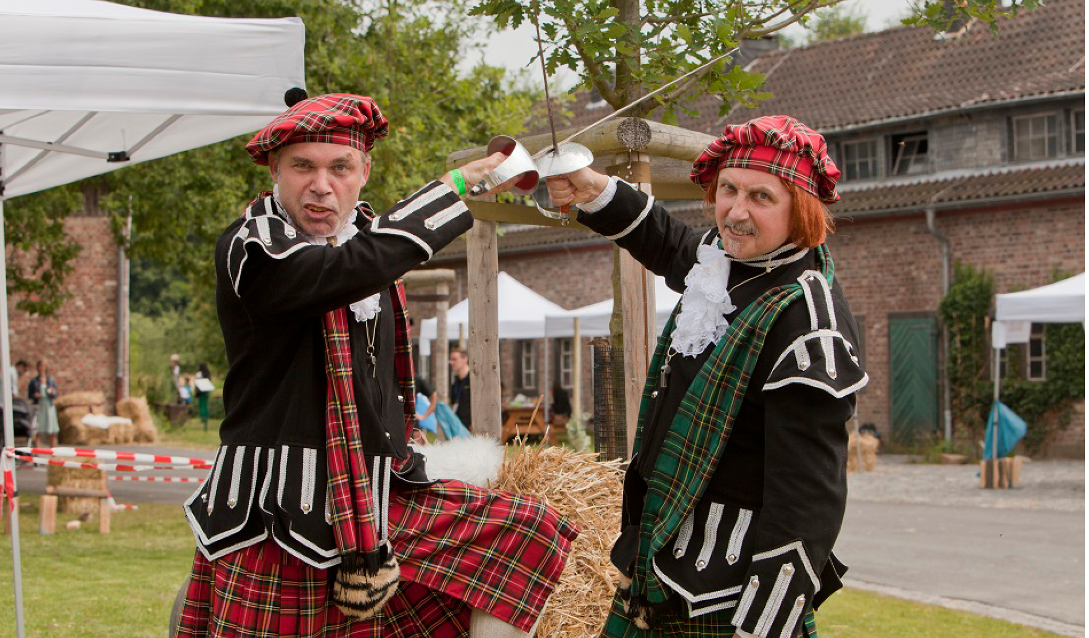 Zwei Teilnehmer der Highland-Games kreuzen in historischen Kostümen die Säbel