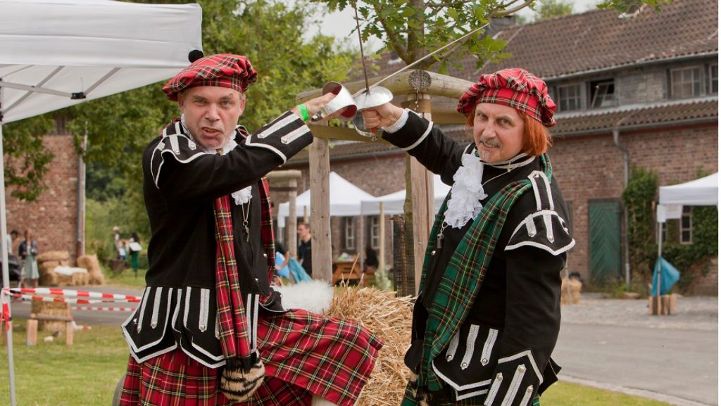 Zwei Teilnehmer der Highland-Games kreuzen in historischen Kostümen die Säbel